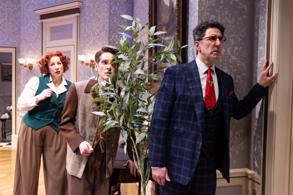 Actors Sean Fortunato, Garrett Lutz, and Katy Sullivan, with their ears pressed to a wall, listening in on a conversation in the next room.