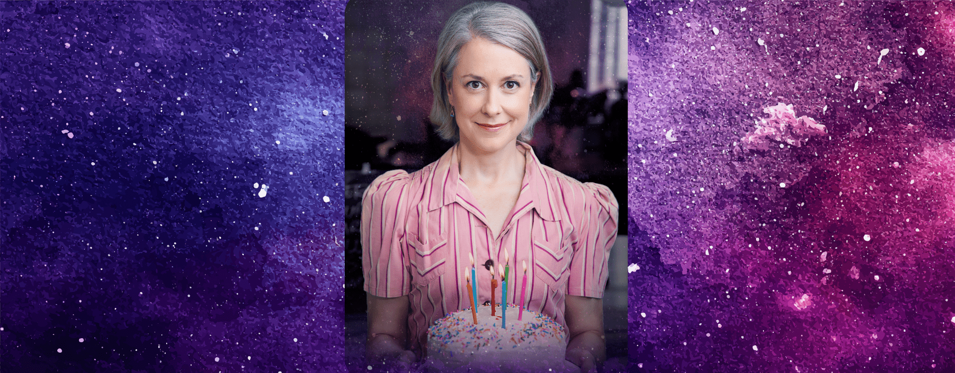 A blonde woman stands in a pink stripped dress holding a birthday cake. She stands in front of a purple galaxy background.