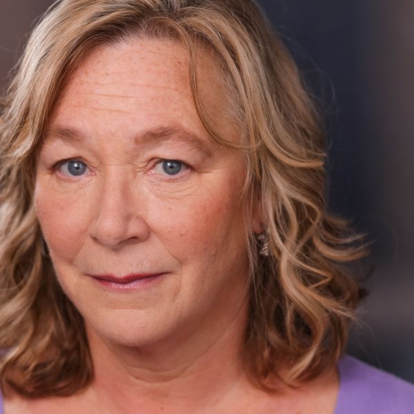Actor Barbara Figgins in a purple shirt, posed in front of a dark gray backdrop