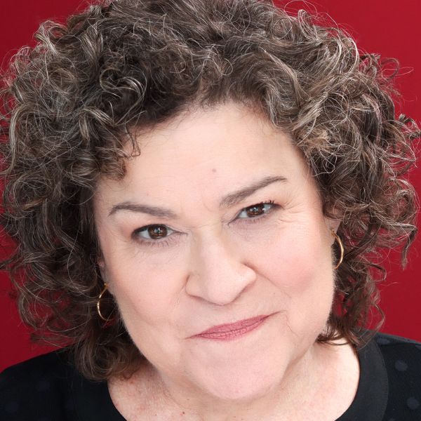 Actress Cindy Gold in a black shirt posed in front of a red backdrop