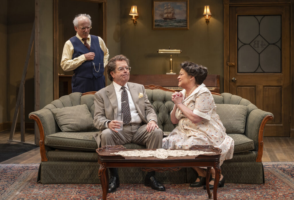 Molly and Jake are seated on a green, victorian style couch while Uncle David stands behind them.