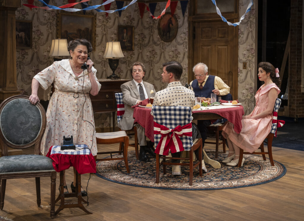 Molly is speaking into an old fashioned telephone, and to her right, her family is seated at a dinner table, watching her take the call.