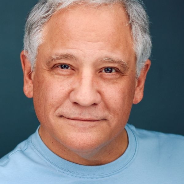 Actor Patrick John Blashill in a blue shirt in front of a dark blue backdrop