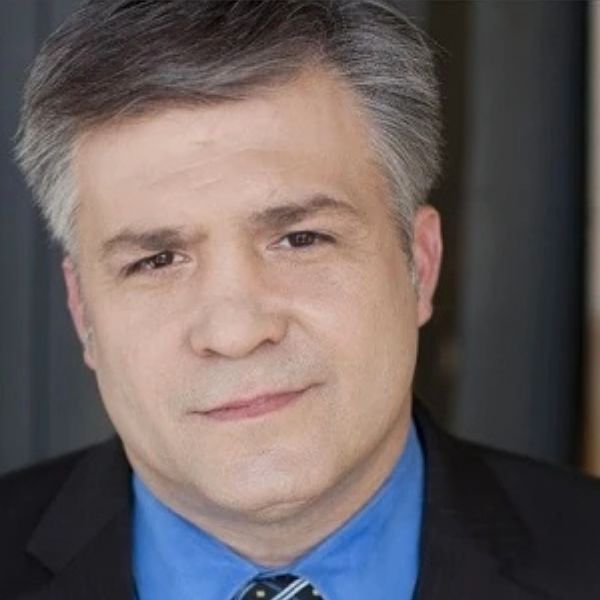 Actor Daniel Houle in a blue shirt and black jacket in front of a grey backdrop