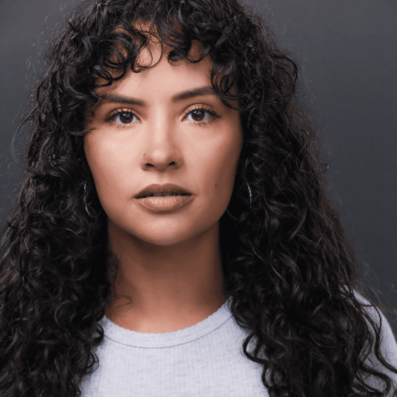 Actress Janyce Caraballo in a light blue shirt, standing in front of a gray backdrop