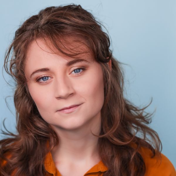 Julia Rowley wearing a n orange shirt, posed in front of a light blue backdrop