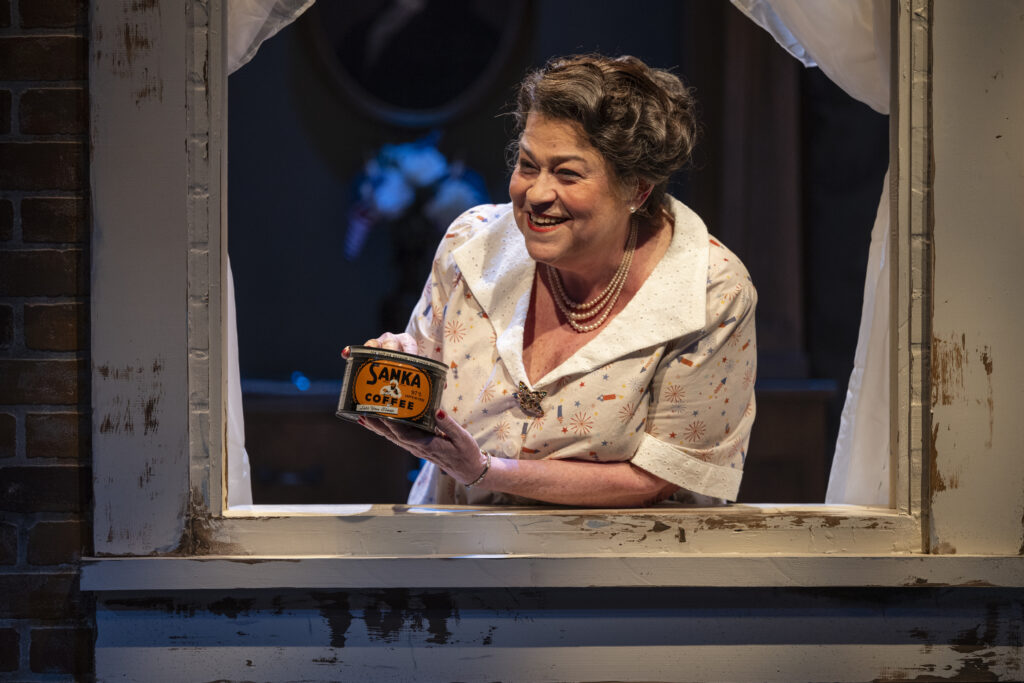 Molly is framed by a window. She leans on the windowsill, holding a can of Sanka brand coffee.