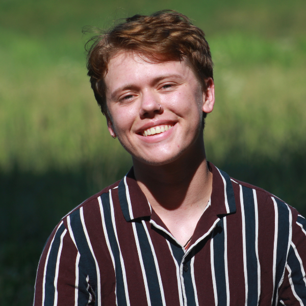 Nick Bartleson posed in front of a green backdrop. He wears a red and blue striped button up shirt.