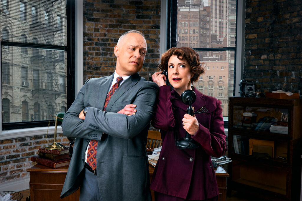 Actors Timothy Edward Kane and Kate Fry posed and holding telephones to their ears as they look over their shoulder at each other