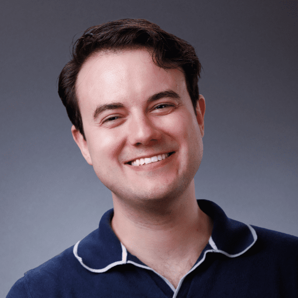 Spencer in a blue shirt posed in front of a gray backdrop