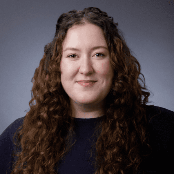Lindsey in a black shirt posed in front of a gray backdrop.