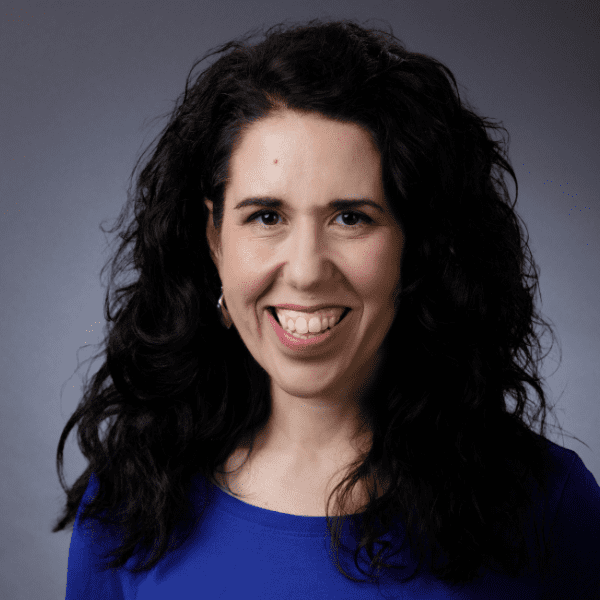 Mara in a blue shirt posed in front of a gray backdrop