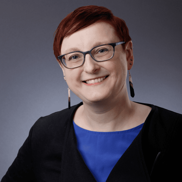 Victoria in a blue and black shirt, posed in front of a gray backdrop