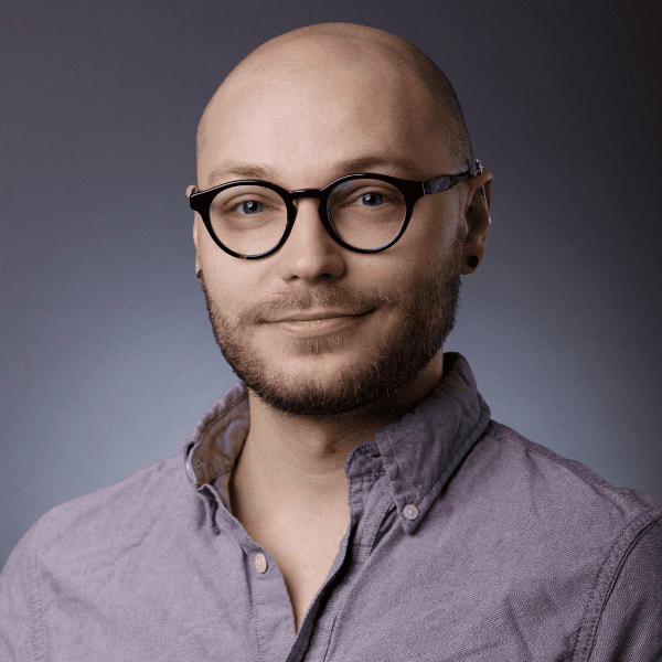 Logan in a purple shirt posed in front of a gray backdrop
