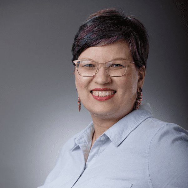Mary in a light blue shirt posed in front of a gray gradient backdrop