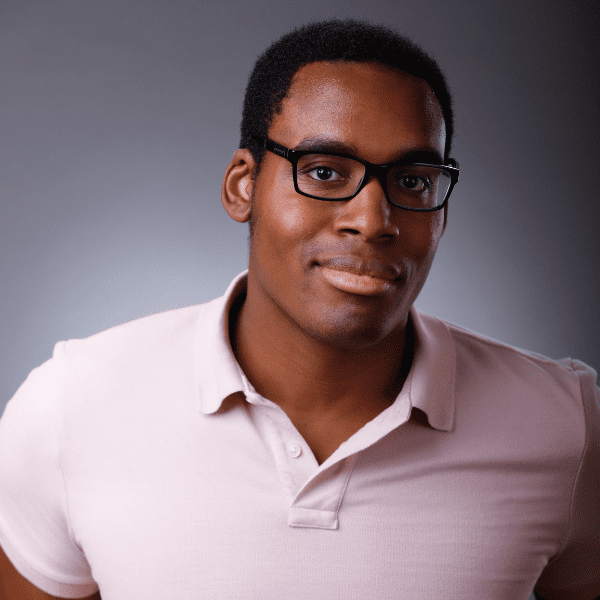 Eric in a pink shirt posed in front of a gray gradient backdrop