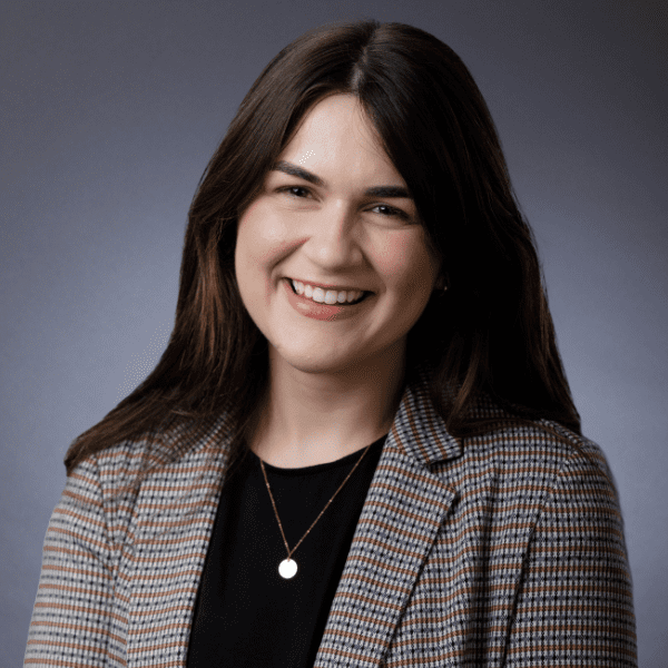 Celine in a black shirt and a gray checkered blazer in front of a gray backdrop.