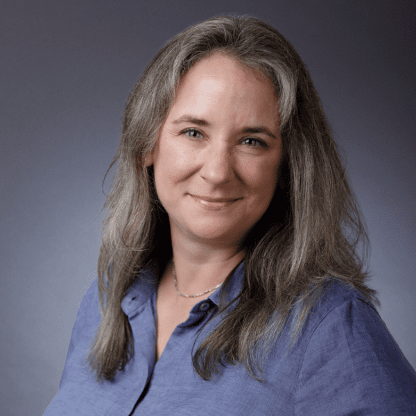 Emily in a light blue shirt, posed in front of a gray background.