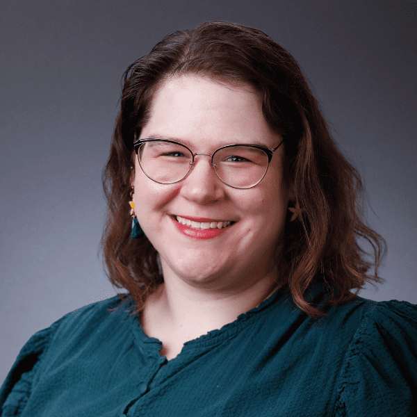 Hannah in a blue shirt posed in front of a gray backdrop.