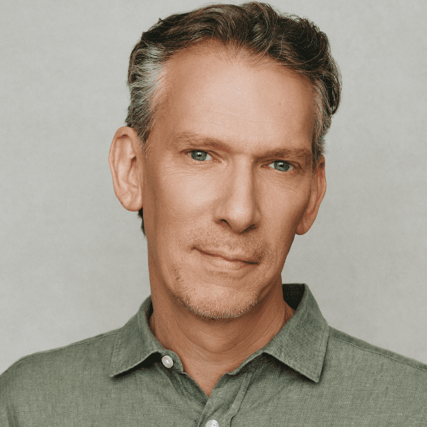 Actor Lawrence Grimm in a green collared shirt in front of a light grey backdrop, pictured from the shoulders up.
