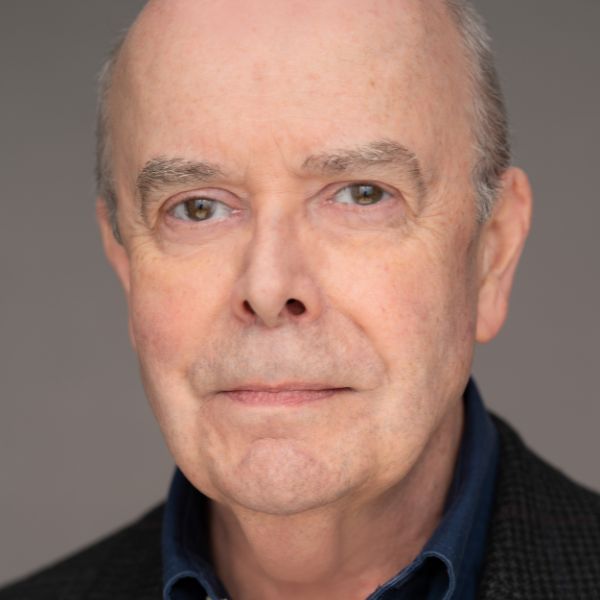 Actor William Dick in a dark blue shirt posed in front of a gray backdrop